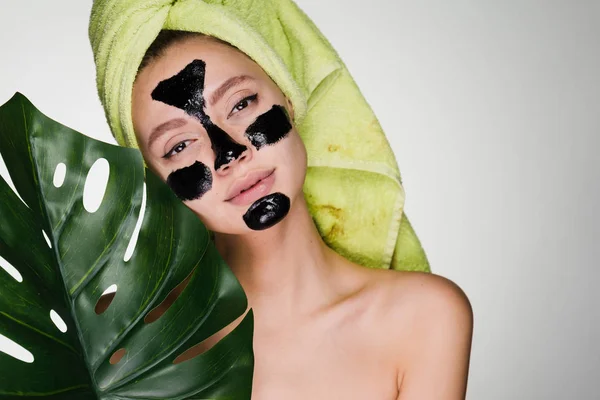 Hermosa joven con una toalla en la cabeza sostiene una hoja verde, máscara negra en las áreas problemáticas en la cara — Foto de Stock
