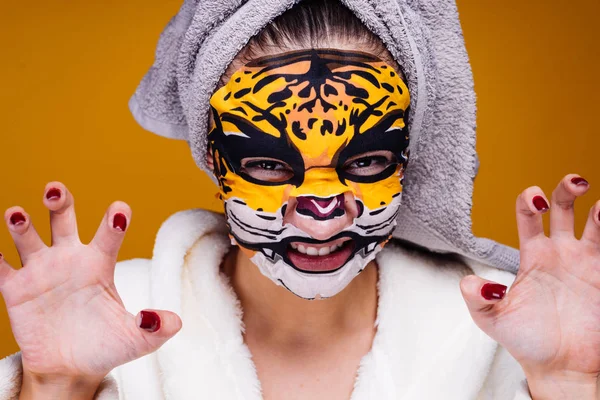 Una joven divertida con una toalla en la cabeza gruñe como un animal, en su cara una máscara con una cara de leopardo — Foto de Stock