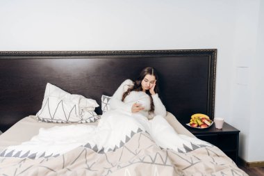 yorgun genç kız işten sonra yatakta yatıyor ve onun smartphone görünüyor