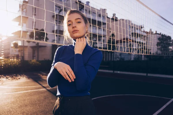 Впевнена стильна дівчина модель в синьому светрі позує на спортивному полі в променях ранкового сонця — стокове фото