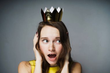 Sarı elbiseli bir genç mavi gözlü kız elleriyle kulaklarını kaplı ve görünüyor şaşırttı, başında altın bir taç