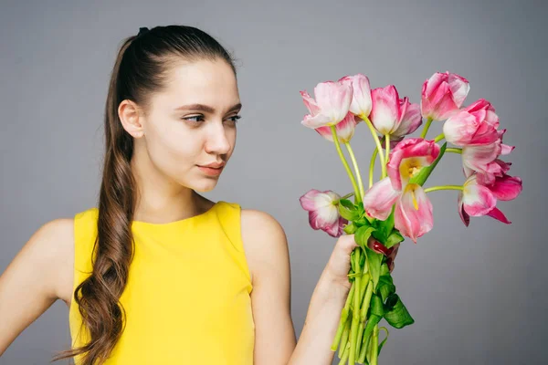Beautiful confident young girl in yellow dress holding bouquet of flowers, enjoying spring — Stock Photo, Image