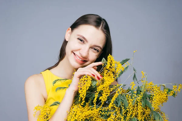 Feliz joven sonriendo, sosteniendo mimosa fragante amarilla y disfrutando de la primavera — Foto de Stock