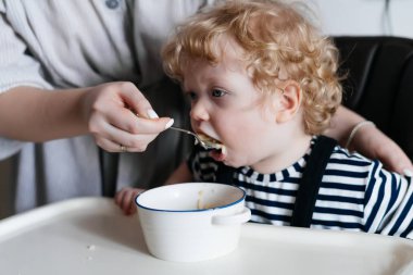 şefkatli anne genç çocuğunu oğlu, bir kaşık, yararlı bir Mısır gevreği ve aile kahvaltı ile beslenir