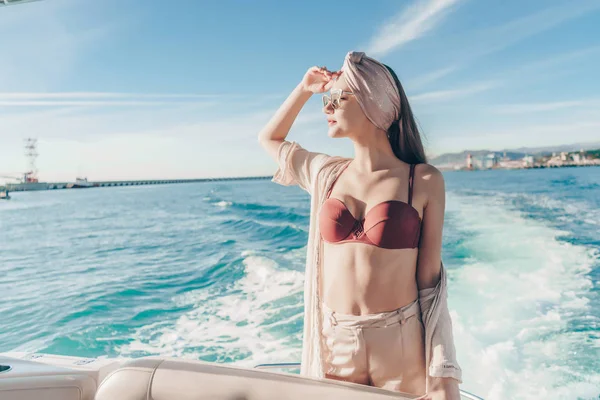 Una atractiva joven con gafas de sol y un traje de baño de moda nada en su yate blanco sobre el mar azul —  Fotos de Stock