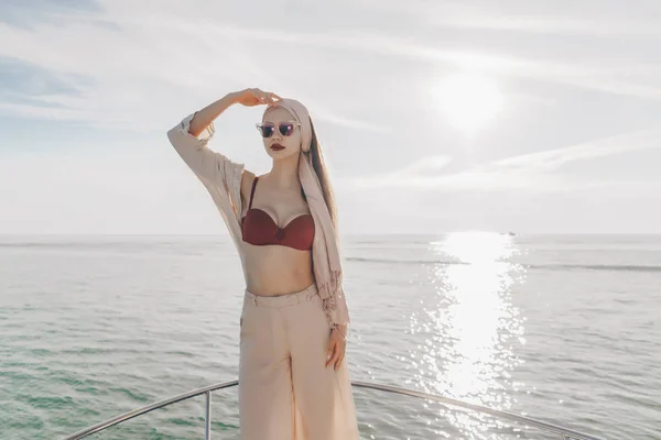 Una joven de lujo en gafas de sol y con un pañuelo en la cabeza viaja por el mar Caribe en su yate blanco, disfruta de una vida rica —  Fotos de Stock