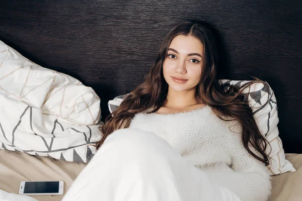 Cute sleepy long-haired girl lying in bed under a white blanket, does not want to go to work — Stock Photo, Image