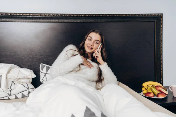 Schattig jong meisje ligt op bed, rust na werk en praten over de telefoon — Stockfoto