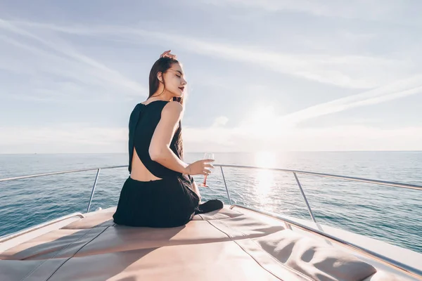 A luxurious attractive girl in a black dress swims on her yacht to the Caribbean islands, drinks champagne — Stock Photo, Image