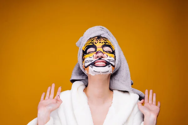 Uma jovem engraçada em um roupão de banho e com uma toalha na cabeça ri, em seu rosto uma máscara com um focinho de um animal — Fotografia de Stock