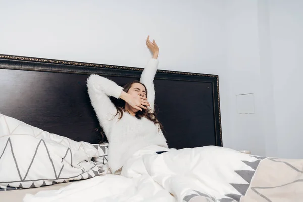 Ein junges Mädchen wacht frühmorgens auf, sitzt im Bett, streckt sich und gähnt — Stockfoto