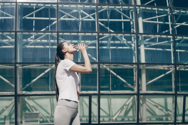 Slank, atletisk jente drikker vann, kommer seg etter en kompleks lang gateøvelse – stockfoto
