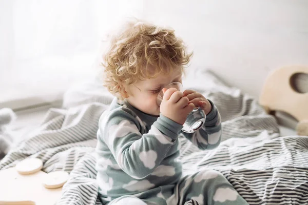 Милий маленький хлопчик сидить на ліжку і п'є воду — стокове фото