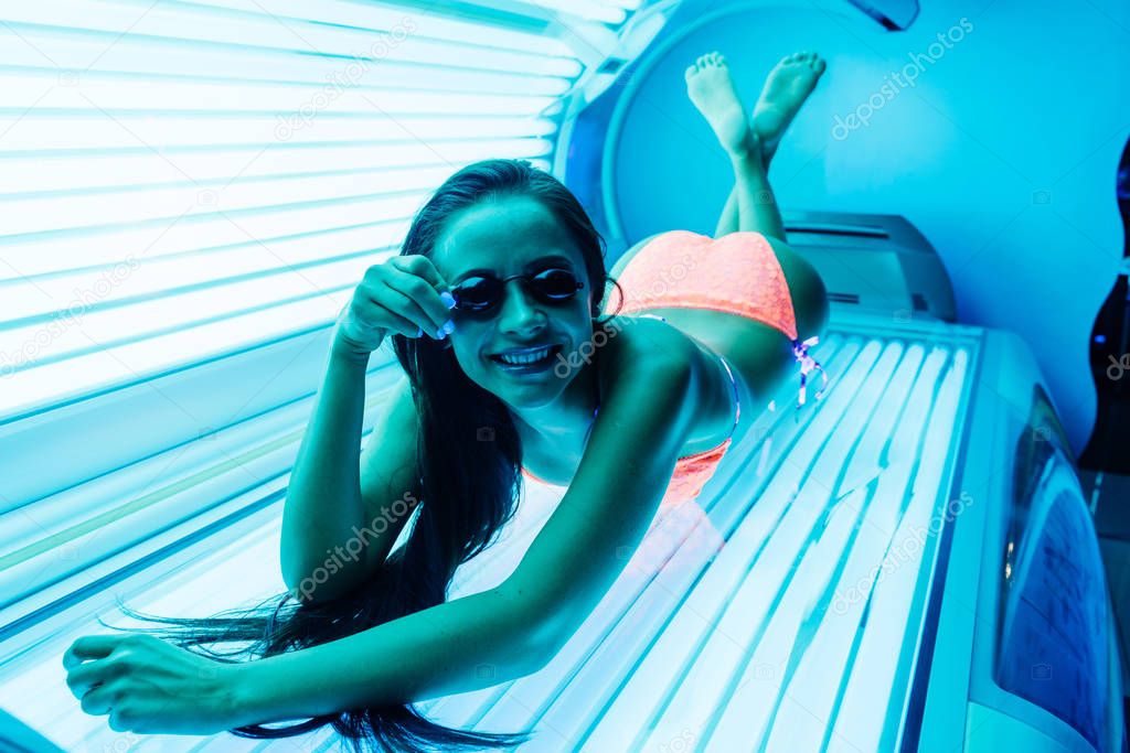 happy young girl in a bathing suit sunbathing in a horizontal solarium under ultra-violet rays, in goggles