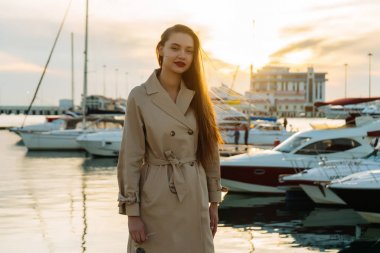 bej moda ceket açık havada akşam güneşin, denizin kenarında yürüyüş güzel uzun saçlı genç kadın gülümseyerek