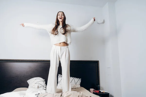 Счастливая девушка в пижаме, прыгающая на кровати, счастливые выходные — стоковое фото