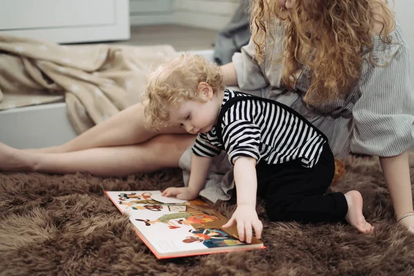 Madre cariñosa juega con su pequeño hijo, su hijo, en casa, leyendo un libro juntos — Foto de Stock