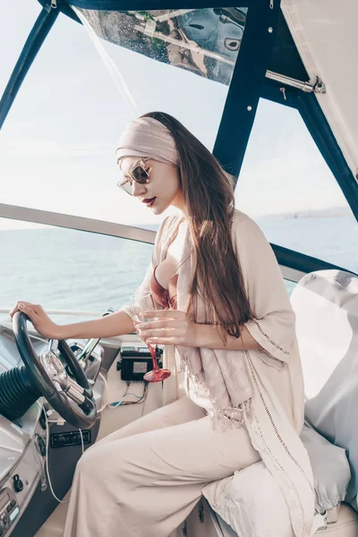 En lyxig ung kvinna kör sin yacht, dricker en cocktail och har ett rikt liv — Stockfoto