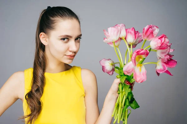 Confident beautiful girl in yellow dress holds a big bouquet of fragrant flowers — Stock Photo, Image