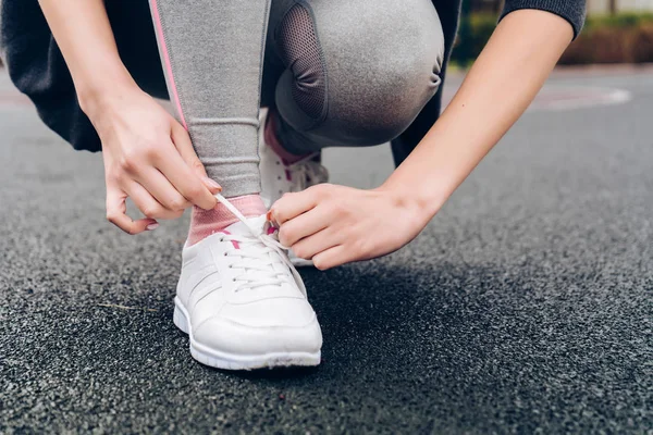 sports young girl trains outdoors, ties up shoelaces on sneakers