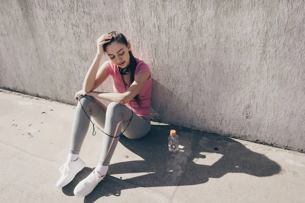 Actieve sporten meisje is rusten na een zware training in de buitenlucht, zittend op de grond en aan kracht te winnen — Stockfoto