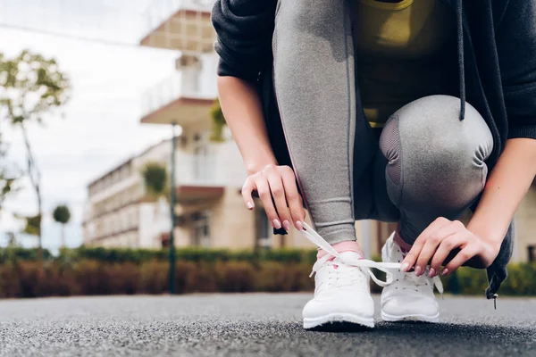 Спортивна молода дівчина наполегливо тренується на відкритому повітрі, зв'язує свої шнурки на кросівках — стокове фото