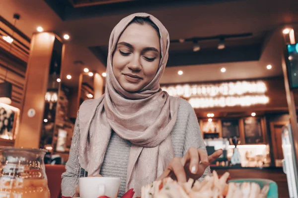 Fejkendő hidzsáb, ül a kávézó és a kávéfogyasztás, aranyos Arab lány mosolyogva — Stock Fotó