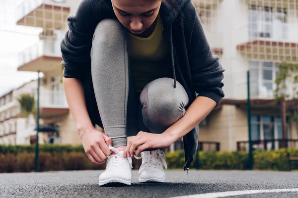 Aktiv ung flicka tåg på en idrottsplats i öppen luft, binder upp skosnören på sneakers — Stockfoto