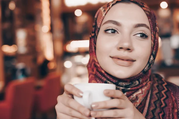 Linda chica musulmana joven con pañuelo en la cabeza, hijab, bebidas delicioso capuchino y sonrisas — Foto de Stock