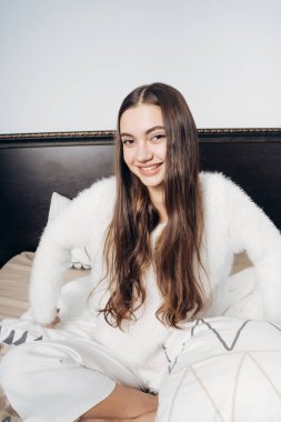 Beyaz bir kazak mutlu uzun saçlı kız yatakta oturur, uyandım, iyi bir sabah sahiptir