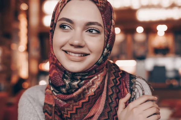 Hermosa chica árabe con pañuelo en la cabeza, hijab, sentado en la cafetería y sonriendo — Foto de Stock