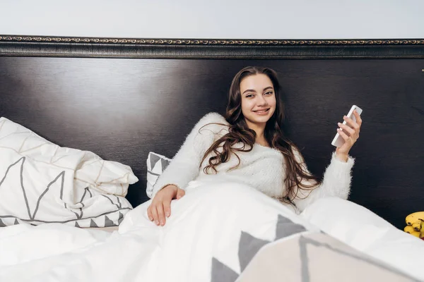 Mooi jong meisje ligt in bed en glimlacht, geniet van een goede morgen — Stockfoto