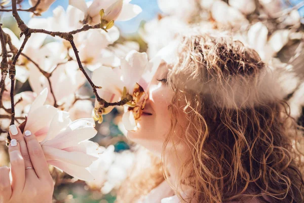 Hermosa chica sonriente huele fragantes flores magnolia, camina en el parque en un cálido día de primavera — Foto de Stock