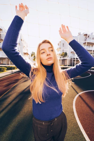 Stijlvolle jong meisje model in een blauwe trui poseren op een sportveld in de zon — Stockfoto