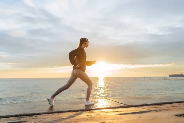 Aktiv ung flicka löpare tränar innan ett långt lopp, vid solnedgång, leder en hälsosam livsstil — Stockfoto