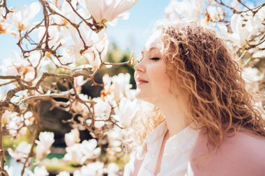 kıvırcık genç kadın güzel kokulu bir çiçek açan Manolya burnunu çekmek, parkta yürüyor