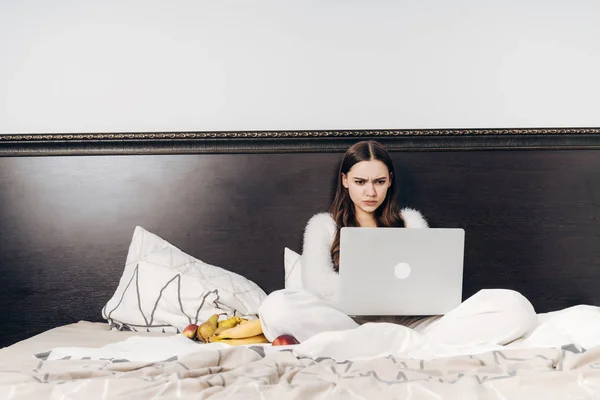 Серйозна стоп-дівчина сидить у ліжку, працює на ноутбуці — стокове фото