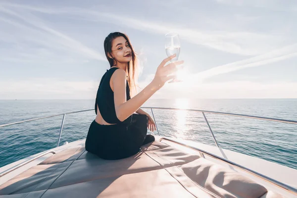 Роскошная длинноволосая девушка в черном платье любит путешествовать на своей яхте по синему морю, пить шампанское и улыбаться — стоковое фото