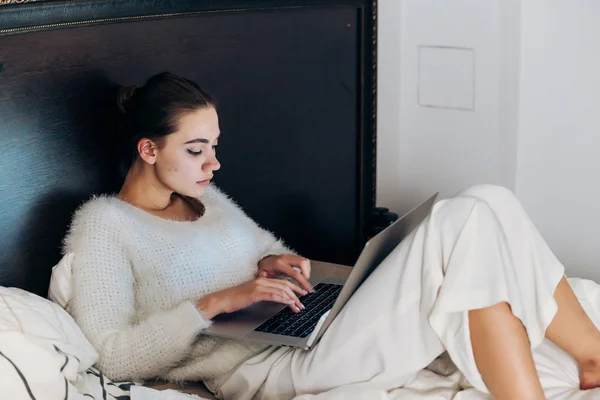 Зосереджена молода дівчина лежить в ліжку і працює на ноутбуці — стокове фото