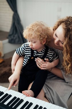 mutlu aile, kıvırcık genç anne küçük oğlu piyano çalmak, birlikte eğlenmek için öğretir.