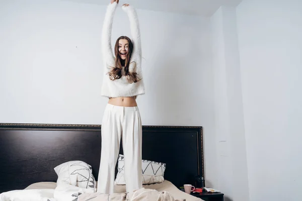 Feliz jovem enérgico em pijama branco pulando na cama no início da manhã — Fotografia de Stock