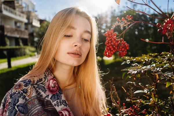 Encantadora chica pensativa rubia con un pañuelo alrededor de su cuello camina alrededor de su jardín en los rayos del sol de primavera, disfruta de la naturaleza y las plantas — Foto de Stock