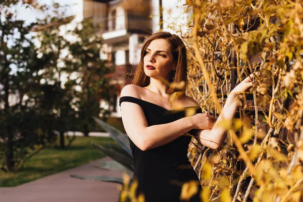 Uma jovem mulher atraente de luxo em um vestido preto andando através de seu jardim nos raios do sol da noite — Fotografia de Stock