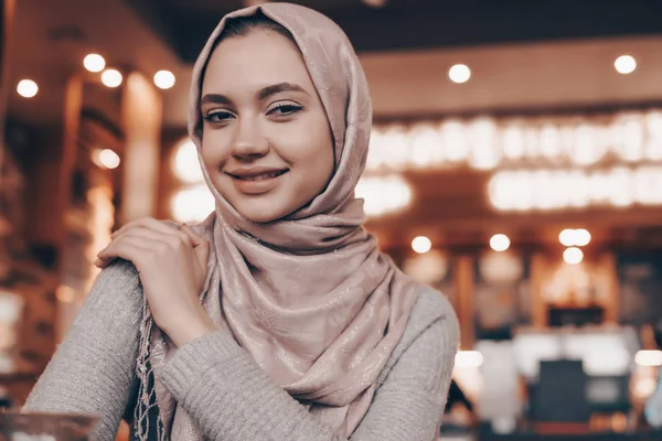 Красивая улыбающаяся арабская девушка в хиджабе сидит в кафе в восточном стиле — стоковое фото