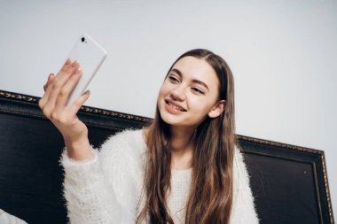 mutlu uzun saçlı kız yatakta işten sonra gülümsüyor oturur ve onu Smartphone'da selfie yapar