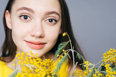 güzel genç kız gülümsüyor ve kamera bakar tutan güzel kokulu sarı Mimoza bir buket