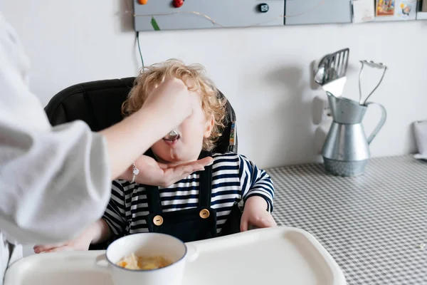 Starostlivá maminka krmí jejího synka kudrnaté s užitečné kaše, rodinnou snídani — Stock fotografie