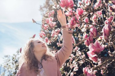 mutlu kıvırcık genç kadın bahar parkta yürüyor, güzel kokulu pembe Manolya sahiptir