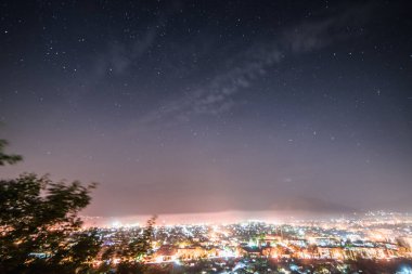 büyük bir şehir birçok parlayan ışıklar ve fenerler gece gökyüzü altında Dağları'nın eteklerinde yukarıdan bir görünüm