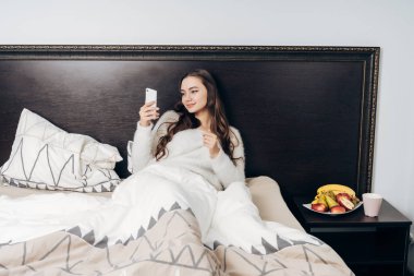 sevimli uzun saçlı kız sabah erken, yatakta yatan gülümseyerek, onun smartphone arıyorum